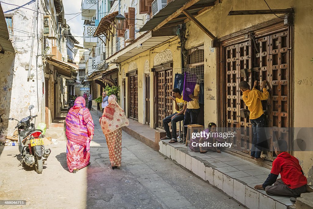 Zanzibar, Tanzania - October 18, 2013: Inhabitants of Zanzibar in an alley of Stone Town. Typical street scene with playing children, two women with their colorful saris walk through the alley.